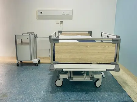 Patientenzimmer in der Solace Clinic in Kabuga In einem großen blauen Patientenzimmer stehen ein Krankenhausbett und ein Nachttisch von Stiegelmeyer.