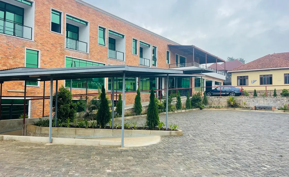 Ansicht der Solace Clinic in Kabuga Der Eingang der Solace-Klinik in der ruandischen Stadt Kabuga liegt an einem gepflasterten Platz. Das moderne Krankenhaus hat eine rote Klinkerfassade und grünes Fensterglas.