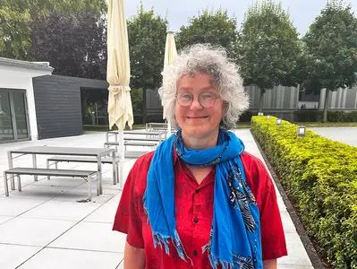 Dr Karen von Hünerbein stoi uśmiechnięta na dziedzińcu budynku administracyjnego Stiegelmeyer w Herford. Ma na sobie czerwoną bluzkę i niebieski szalik.