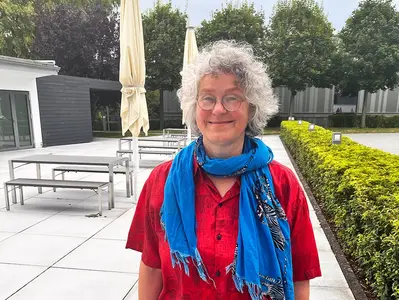 Dr Karen von Hünerbein stands smiling in the courtyard of the Stiegelmeyer administration building in Herford. She is wearing a red blouse and a blue scarf.