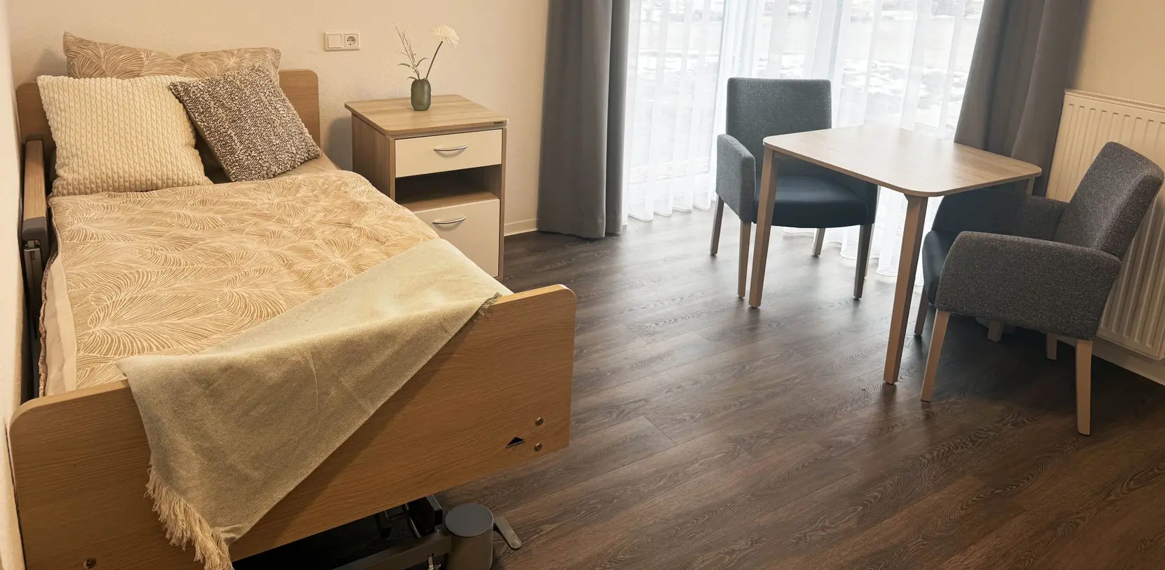 Modern eingerichtetes Bewohnerzimmer mit wohnlichem Pflegebett von Stiegelmeyer, Nachttisch und Sitzbereich in einer compassio Seniorenresidenz