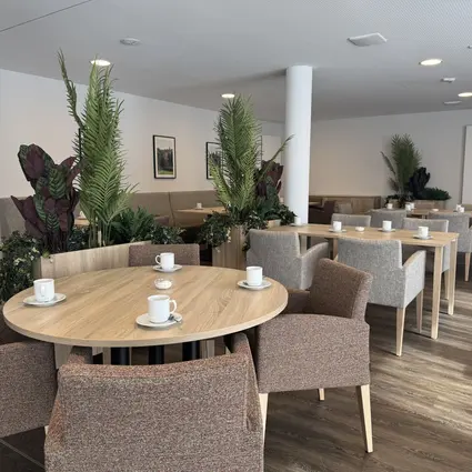 A welcoming restaurant area with tables, armchairs and plants in a compassio care home