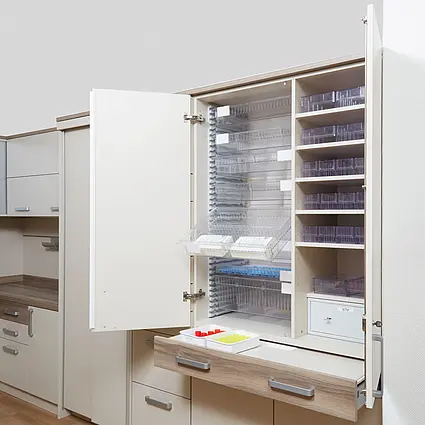 Armario para medicamentos en la sala de servicio Armario para medicamentos de Stiegelmeyer en una sala de servicio con superficie de trabajo y espacio de almacenamiento para utensilios de cuidado.