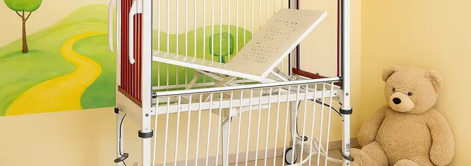 In einer mit KI generierten Skizze steht das Kinderbett mit roten Kopf- und Fußteilen vor einer gelben Wand mit einem gemalten Landschaftsmotiv. Neben dem Bett sitzt ein großer Teddybär auf dem Fußboden.