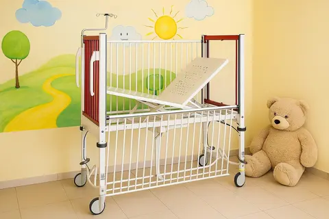 In einer mit KI generierten Skizze steht das Kinderbett mit roten Kopf- und Fußteilen vor einer gelben Wand mit einem gemalten Landschaftsmotiv. Neben dem Bett sitzt ein großer Teddybär auf dem Fußboden.