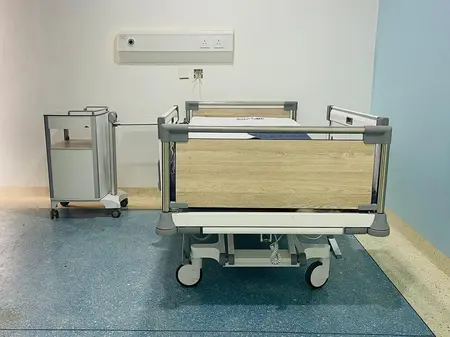A hospital bed and a bedside cabinet from Stiegelmeyer are located in a large blue patient room.